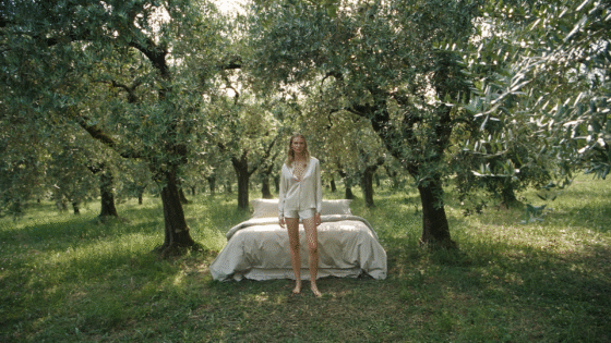 bed made up with Frette bed linen in the middle of olive grove with model in Frette bed wear