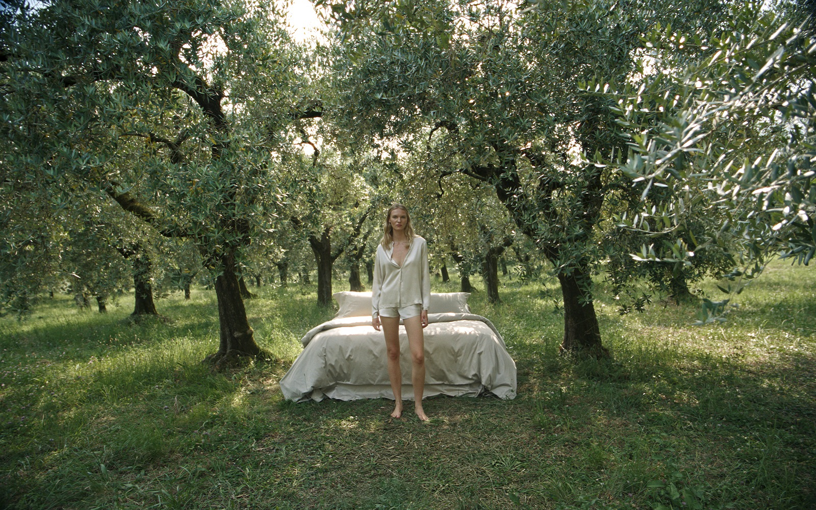 bed made up with Frette bed linen in the middle of olive grove with model in Frette bed wear