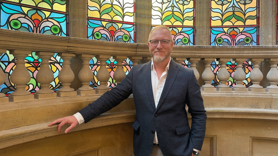portrait of Ray Goertz next to stained glass window on stairway of Hobson Cambridge by Adina