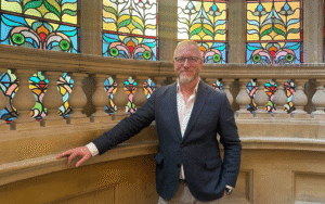 portrait of Ray Goertz next to stained glass window on stairway of Hobson Cambridge by Adina