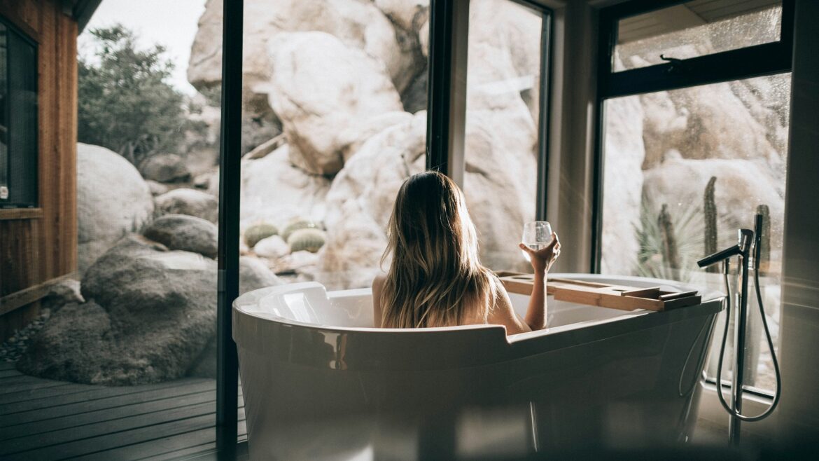 person in luxury soaking bath with a glass of wine and surrounded by natural rock