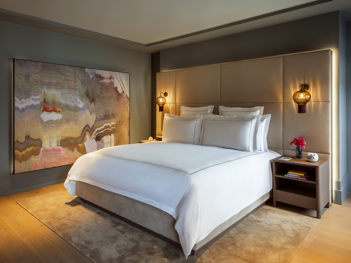 guestroom in rosewood amsterdam with bespoke headboard and lighting behind the bed and painting on wall facing the bed