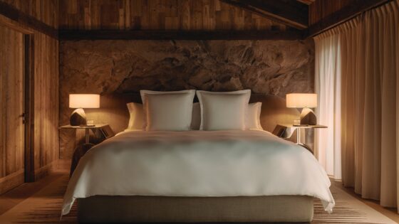 double bed with white linen against stone wall and wooden ceiling in rosewood courcheval