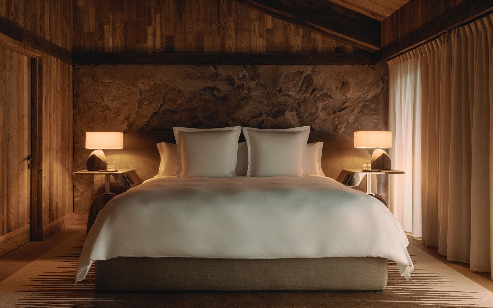 double bed with white linen against stone wall and wooden ceiling in rosewood courcheval