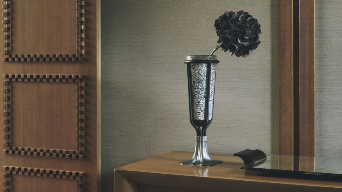 vase on wooden surface with single black flower