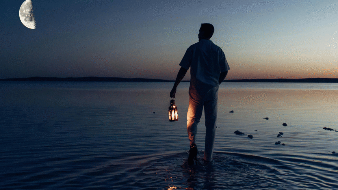 Man walking in the sea at dusk, beneath half moon