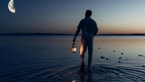 Man walking in the sea at dusk, beneath half moon