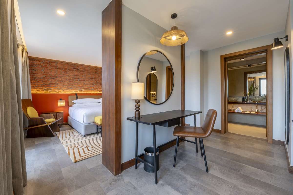 hotel guestroom with exposed brick wall behind the bed and separate work space and desk