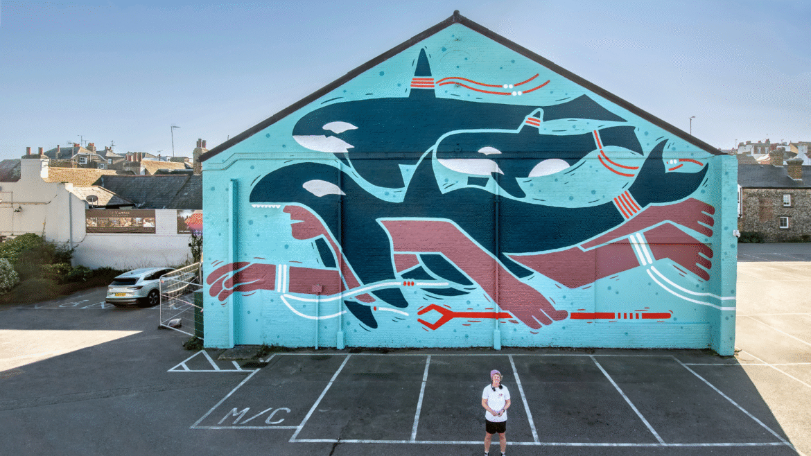 Creative Debuts artist in front of exterior mural showing swimmer and orca