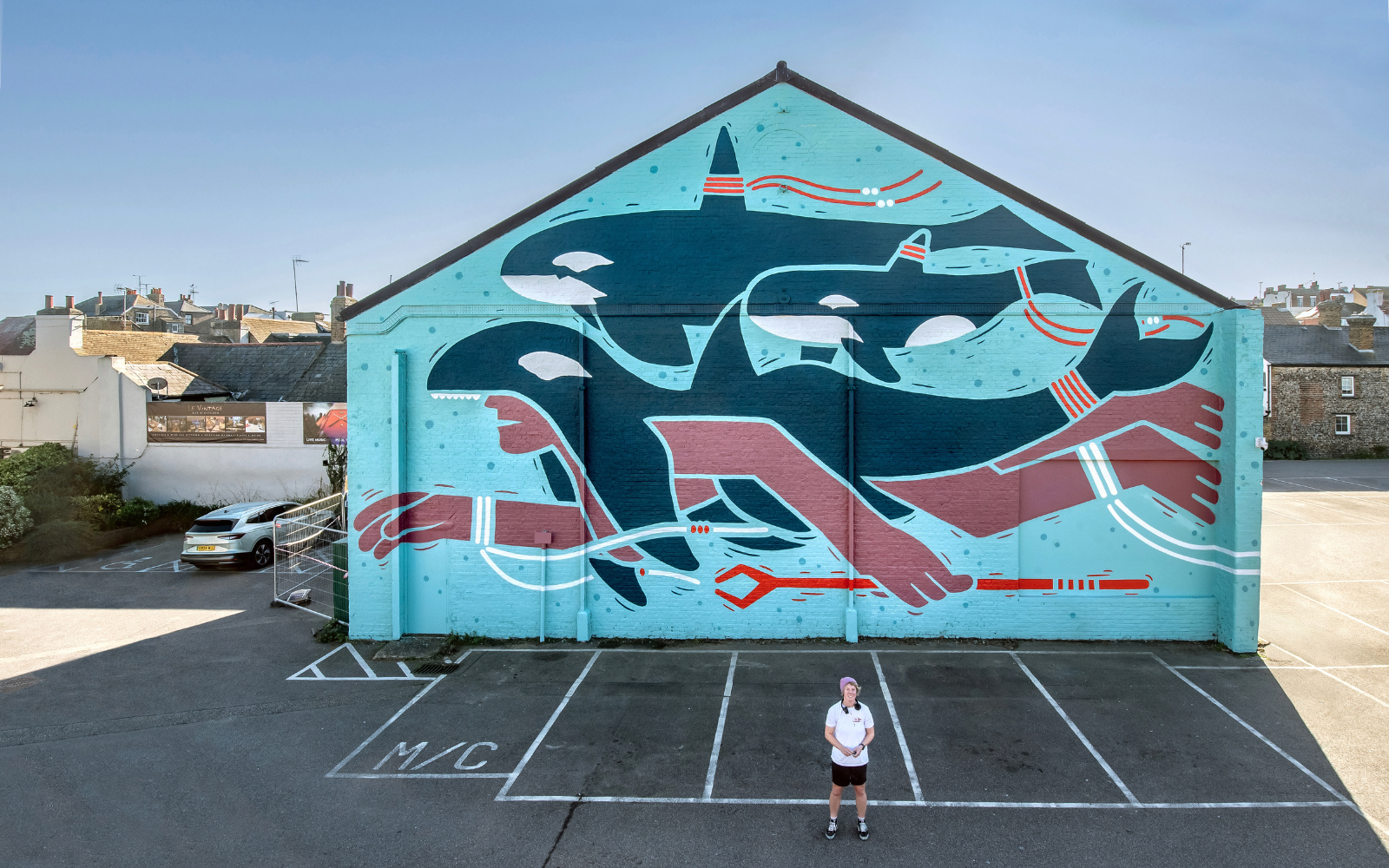 Creative Debuts artist in front of exterior mural showing swimmer and orca