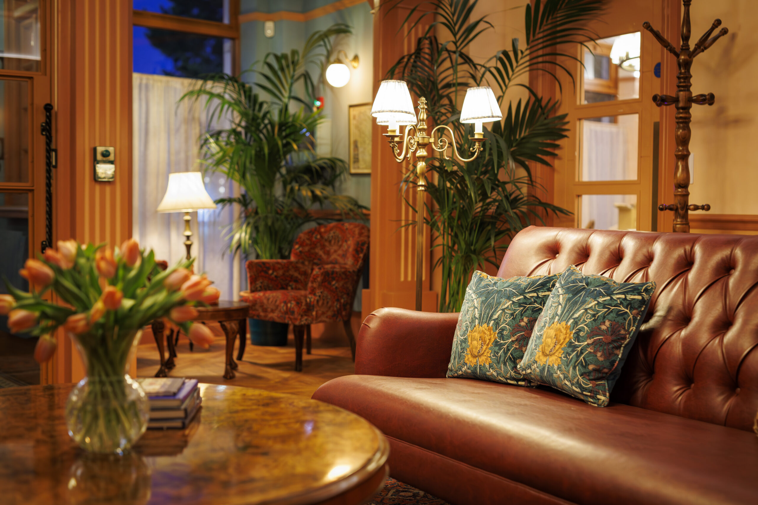 Warm toned room with light wood accents and tan chesterfield sofa. Pillows in Morris & Co. fabric