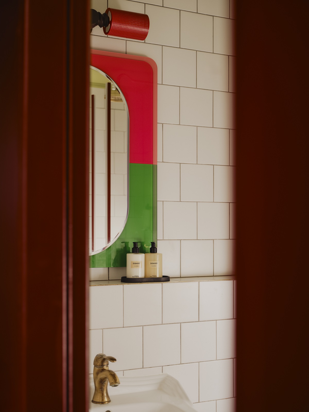 view into the bathroom with white vintage tiles and bright orange and green mirror frame in The_Dean_Berlin_