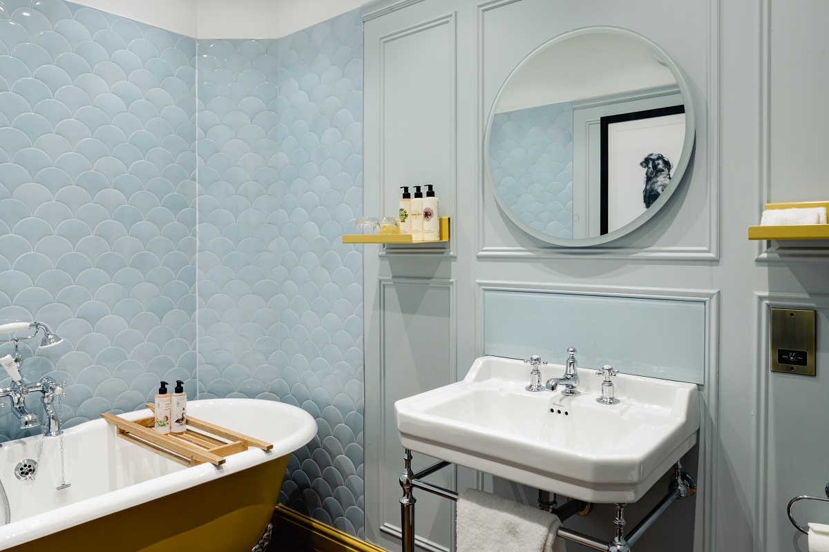 bathroom with light blue scalloped tiles and roll top bath with yellow surround from House of Rohl