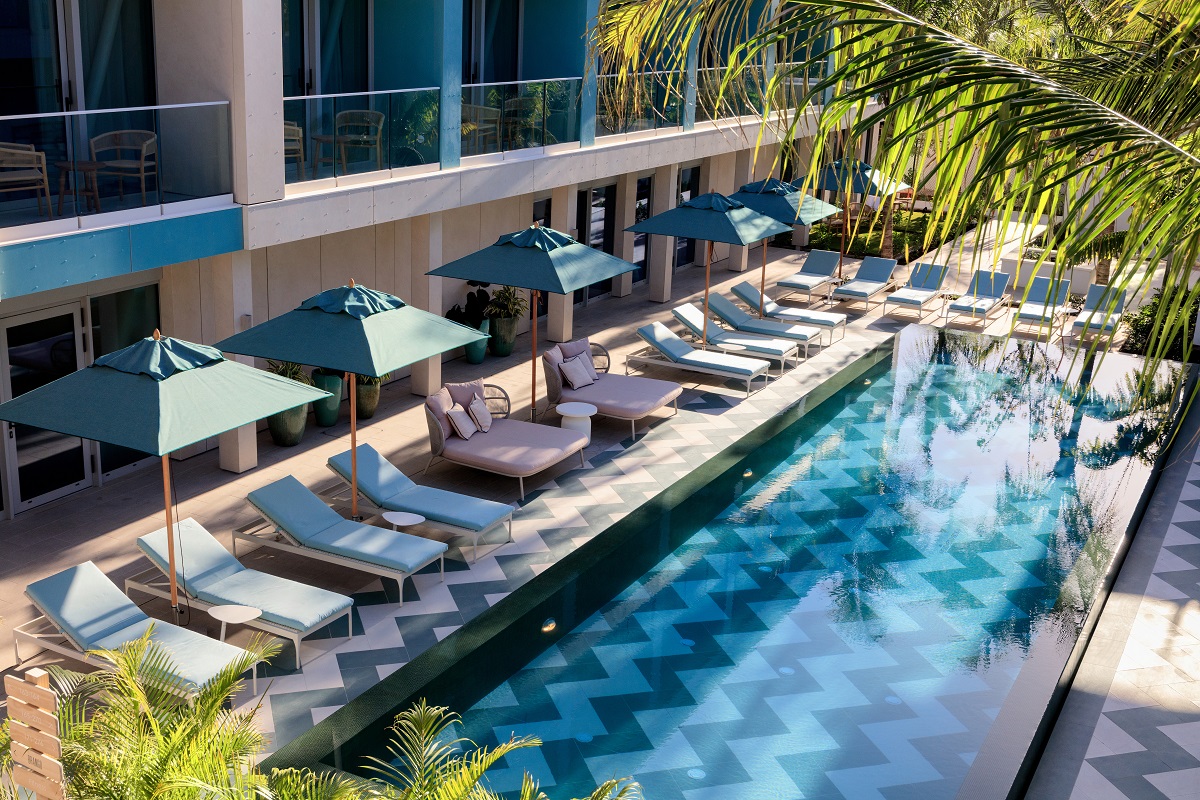 swimming pool with checked tiles surrounded by sunloungers and palm trees