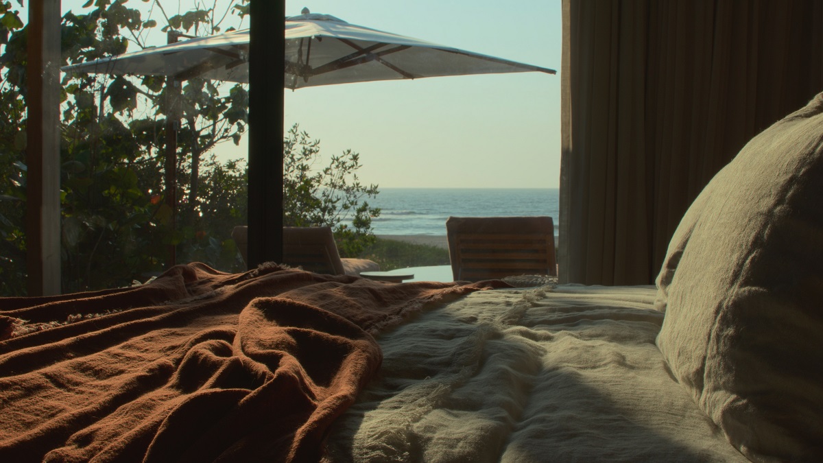 unmade bed with view across terrace to sea