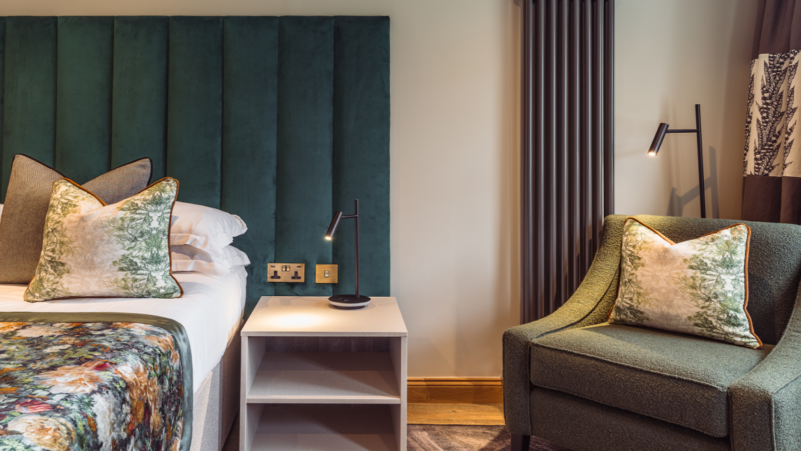 green upholstered headboard in hotel guestroom with Hamilton Litestat fittings
