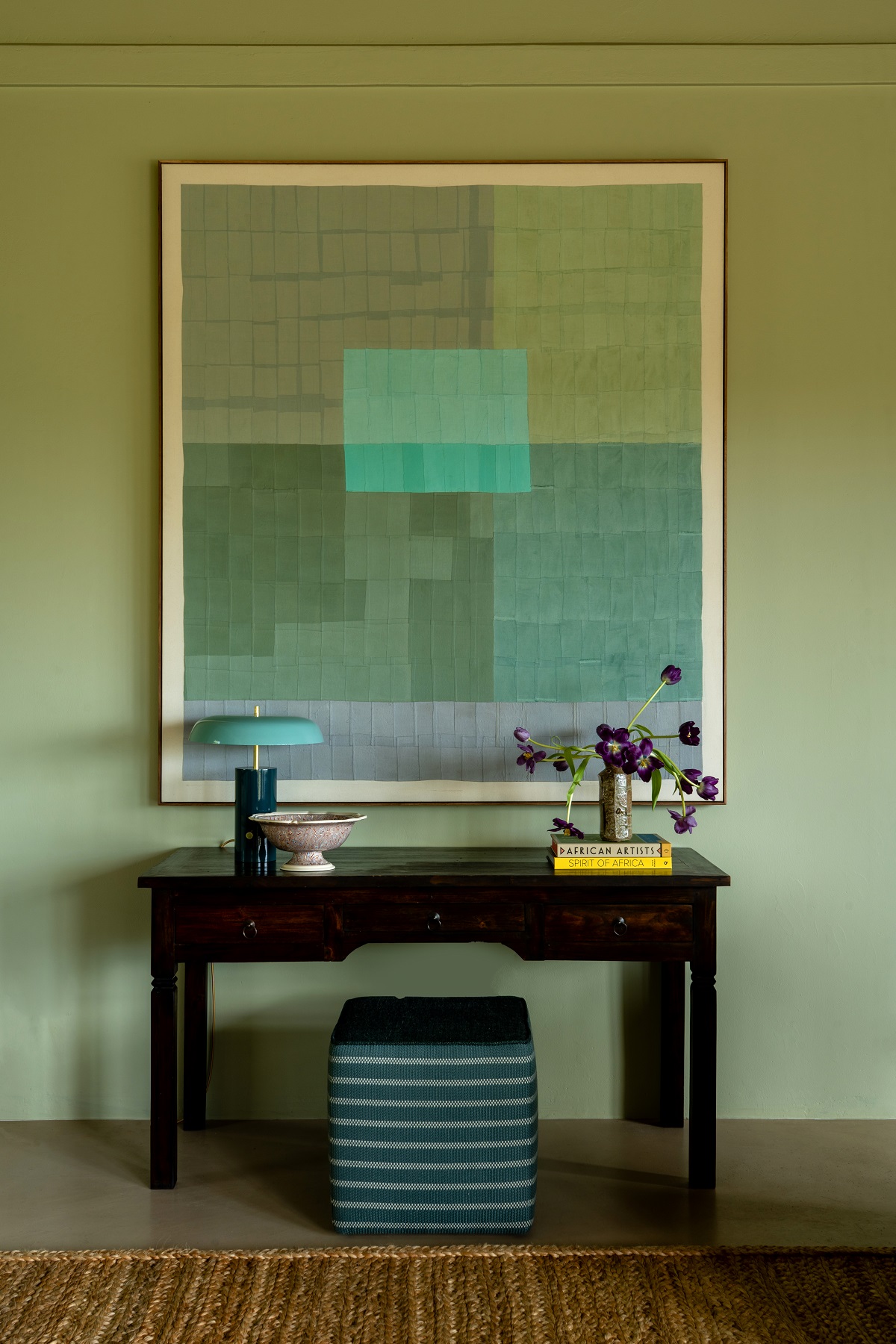 detail of wooden table against green wall with abstract art work above in same colour tones