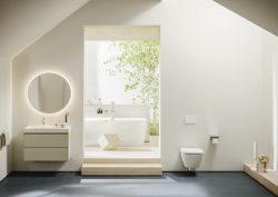 bathroom vanity and toilet with door leading into space with freestanding bath by Laufen