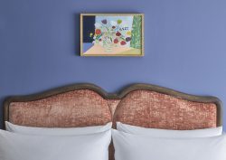 blue wall and coral upholstered headboard with white pillows and art on the wall at the Broadwick Soho