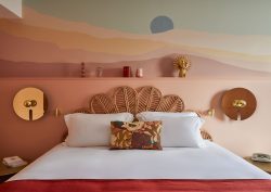 sunset tones mural painted on the wall behind a bed with a wicker headboard and brass sidelamps in hotel Indigo bordeaux
