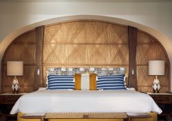 Maroma hotel bed set into arched alcove with a wicker woven headboard behind, blue striped pillows and ceramic bedside lamps