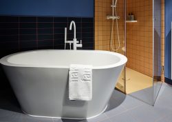 Freestanding Bette bath in 25hours bathroom with yellow shower cubicle and blue walls