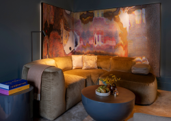 Dark, ashy purple walled seating area at The Rosewood Amsterdam. A multi-coloured watery paint painting hangs behind a mustard toned mid-century design sofa.