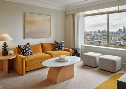 Lounge area in guest bedroom of Hilton Park Lane. Large window shows views across London while a yellow sofa is positioned besides a side table with Northern Lights ceramic lamp