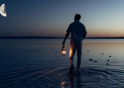 Man walking in the sea at dusk, beneath half moon