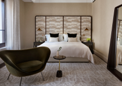 Neutral-toned bedroom, mid-century modernism in design, in The OWO Residences by Raffles. Textured headboard frames the bed, while a tall mirror leans against the wall to the right and a organic shaped armchair sits to the left of the bed. By StudioMorey