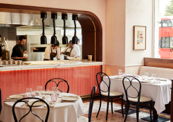 Leydi restaurant at Hyde Hotel London, with pink tiled open kitchen and french bistro style chairs around round tables with white table cloth