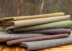 a stack of boucle fabrics on a wooden table from the Gaia range by Skopos