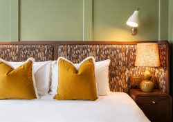olive green panelled wall with patterned fabric headboard and mustard yellow cushions in Mollies Manchester