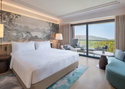 kingsize bed with white linen with views across tropical hillside in guestroom in JW Marriott in Goa