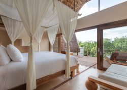 bed draped in fabric with white linen looking out over the Tulum jungle treetops at La Valise