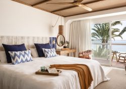 view across double bed with brown throw and blue cushions to windows and seaview in guestroom in Zel Mallorca