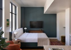 aparthotel guestroom suite with bed in front of dark blue wall and plants in the foreground