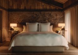 double bed with white linen against stone wall and wooden ceiling in rosewood courcheval