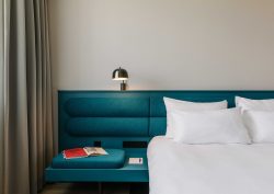 blue headboard and bed side table with book and light and white linen on bed
