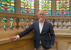 portrait of Ray Goertz next to stained glass window on stairway of Hobson Cambridge by Adina