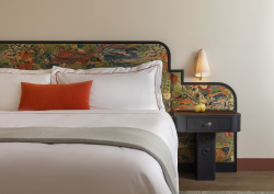 detail of bed with white linen, orange cushion and mid century design upholstered bedhead in Hotel Daphne from Bunkhouse