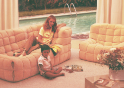 pastel-hued photograph of mother laying on a Kashima sofa by Ligne Roset, with child reading magazine on floor beside her
