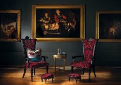 black wall with period paintings in gold frames behind black and red ststement chairs in room designed by Blackpop